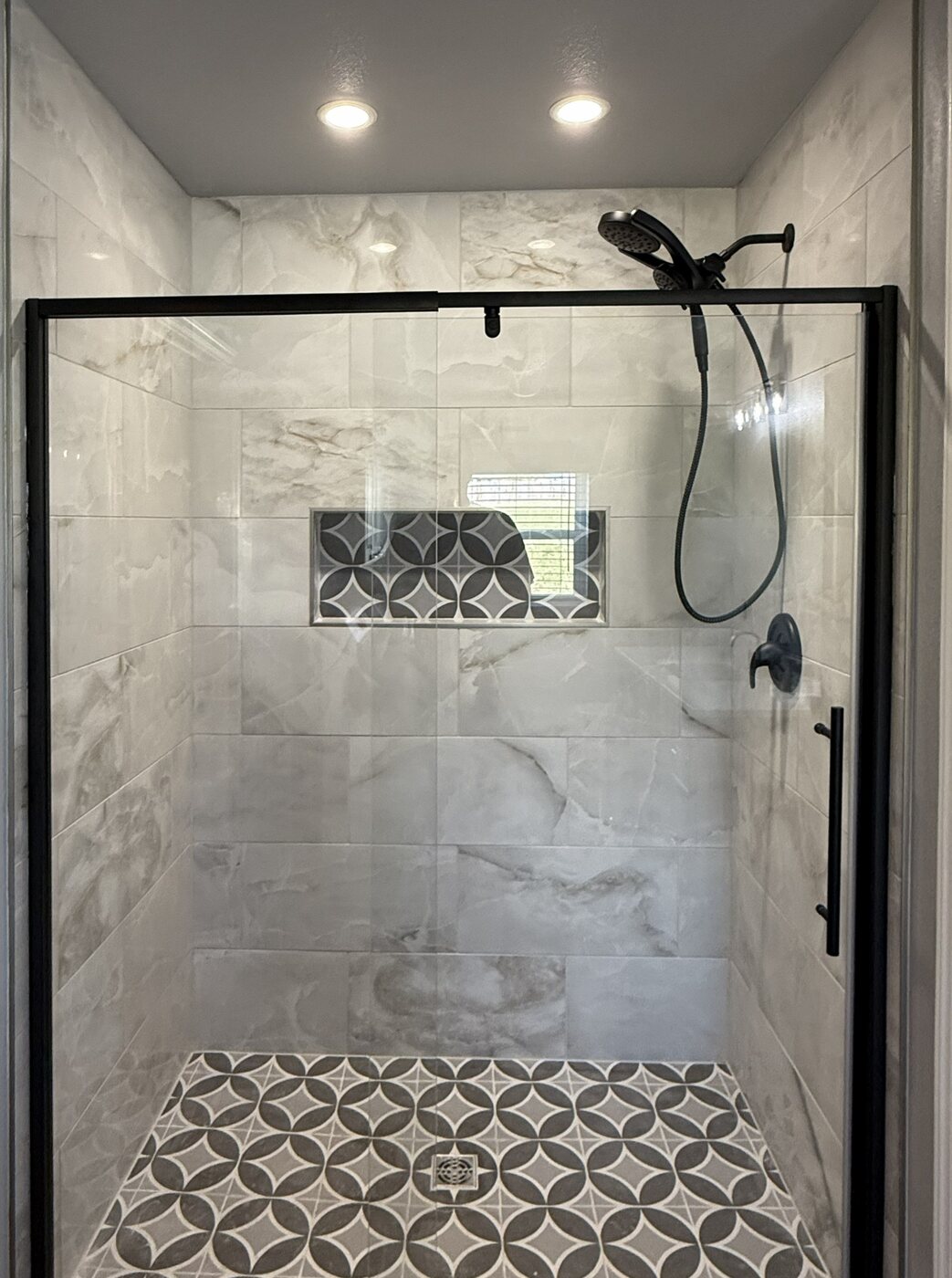 Custom tiled shower with black-framed glass and patterned niche
